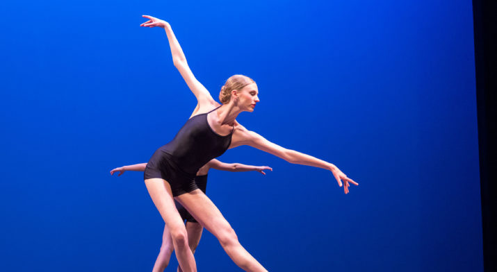 ballerina posing on stage in front of blue background.