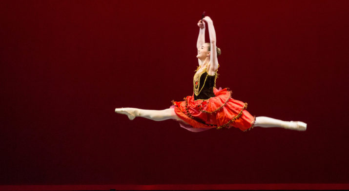 dancer in red skirt mid jump on stage.