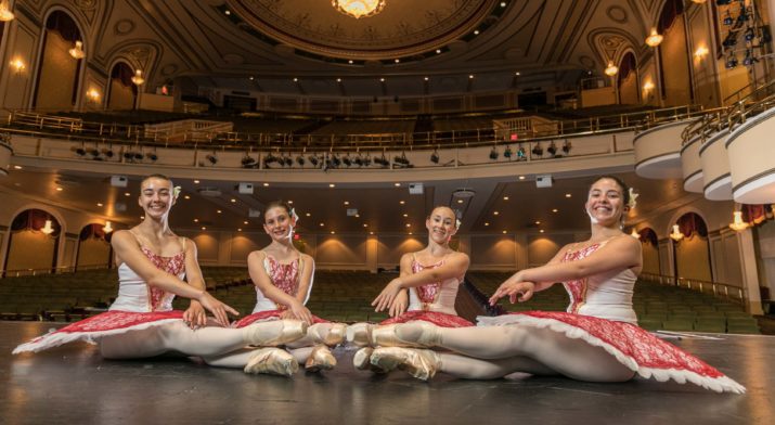 young ballerinas sitting on stage in auditorium.