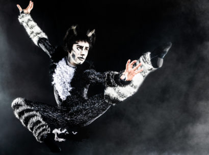 A performing in the musical cats in full makeup jumping.