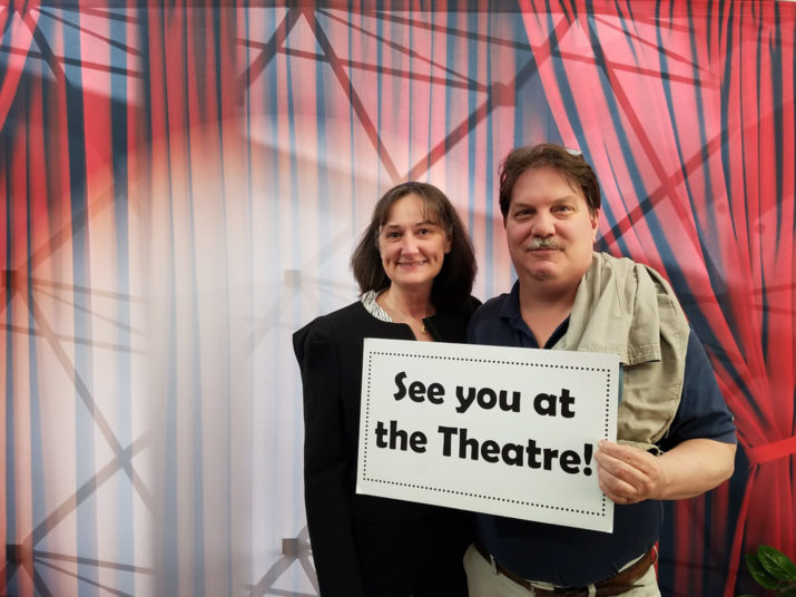 couple holding a sign that says see you at the theatre.