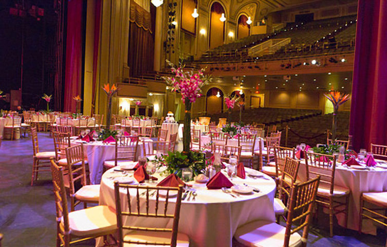 tables and chairs set out for a corporate dinner on a stage.