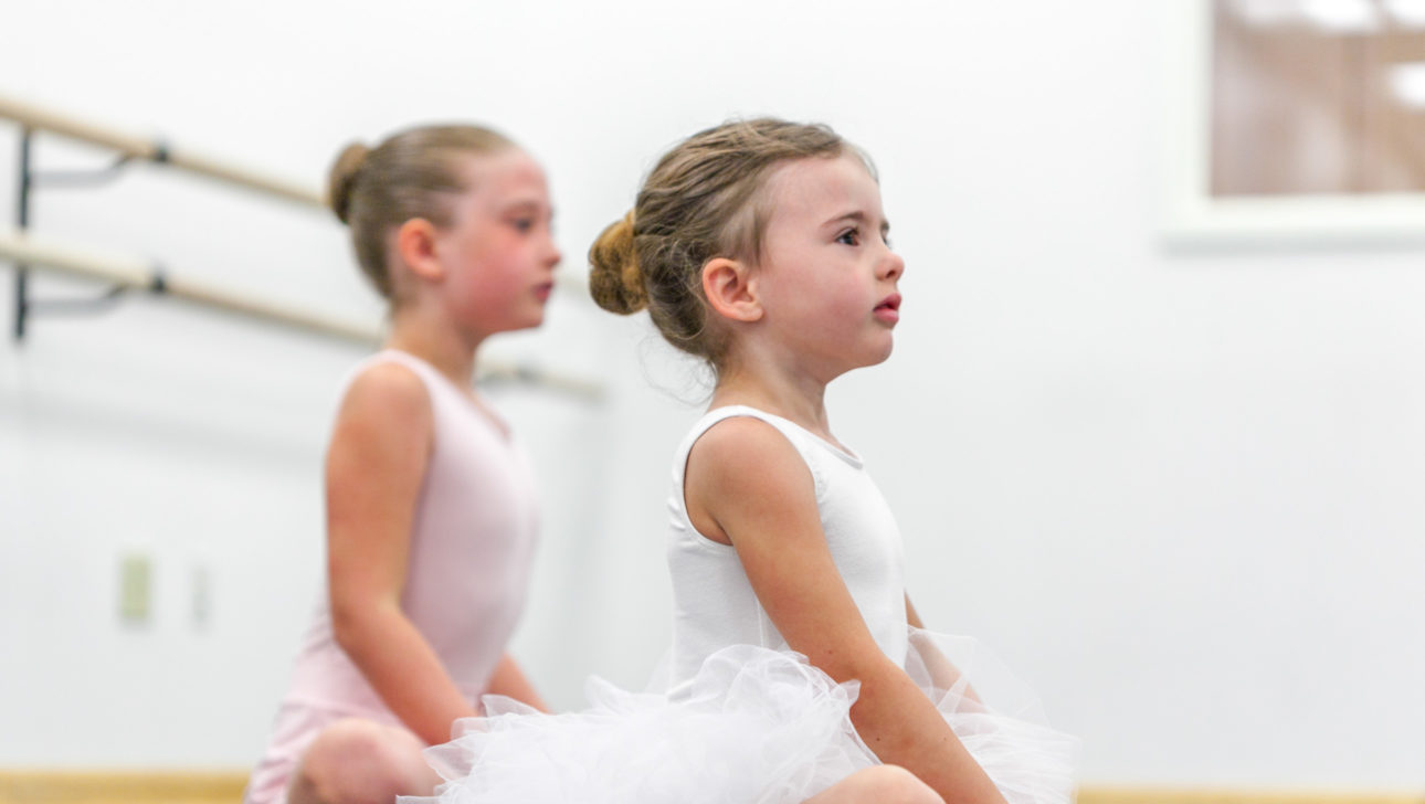 two young ballerinas sitting on floor.