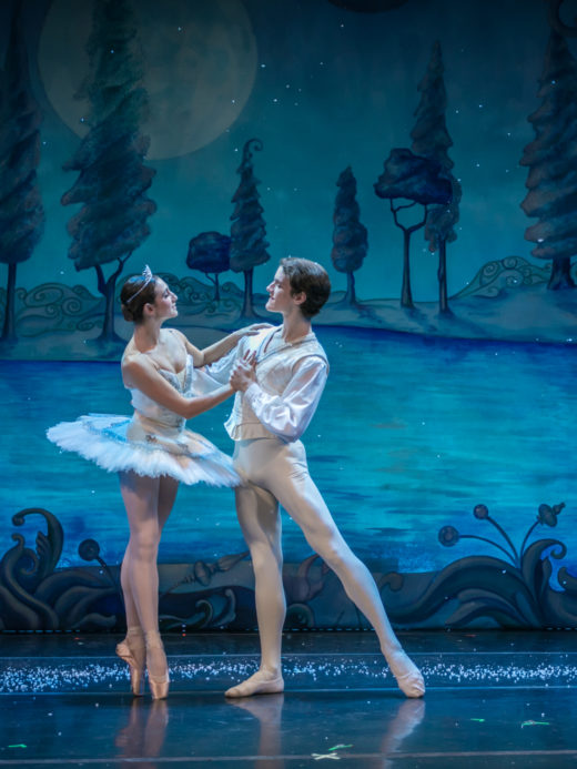 male and female ballerina on stage in front of blue background.