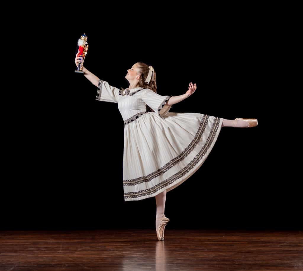Morgan Soulé is posed in an arabesque. holding a Nutcracker before her. 