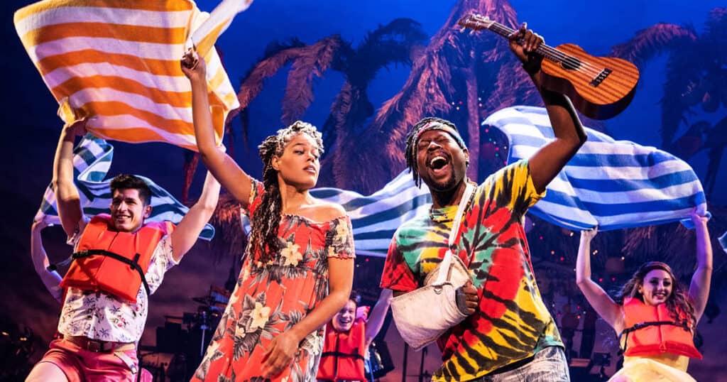 Marley (Rachel Lyn Fobbs) is dancing beside Jamal (Matthew James Sherrod). She is swinging a towel above her head, mirroring Jamal's arm, which is holding a ukulele above his head as he sings. Marley, wearing an off-the-shoulder tropical-print dress, is dancing next to Jamal, wearing a tie-dye shirt with his arm in a sling. The company behind them, all wearing life jackets, are waving towels in the air as they dance in the background.