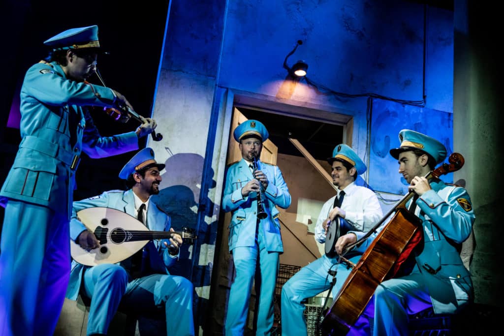 The cast of The Band's Visit playing instruments in a rustic doorway. 