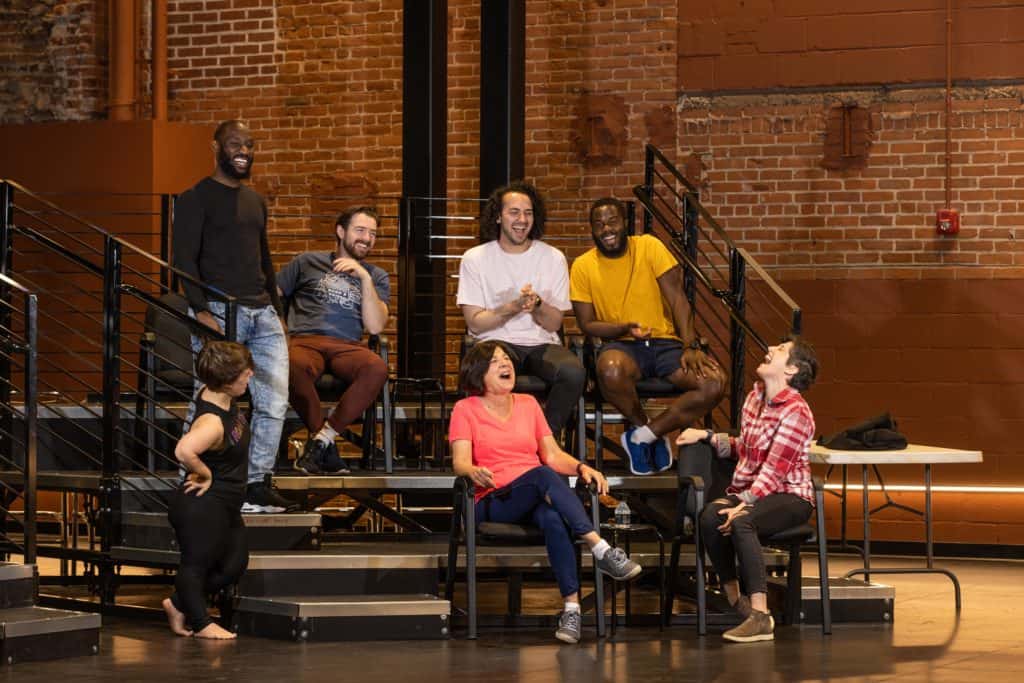 The Worc at Play Program participants sit in the BrickBox Theater. They are sitting in front of an exposed brick wall sitting on risers and are laughing and smiling.