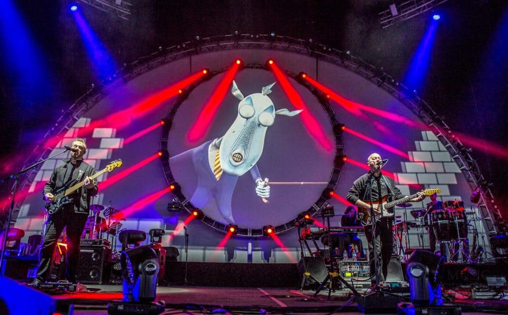Members of Brit Floyd are playing their instruments mid song with an image of a robotic corporate dog casted on the screen behind them. Red lasers are also casting from behind.