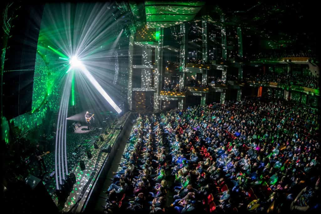 A view of the audience with an array of dotted multi-colored lights cast among the crowd.