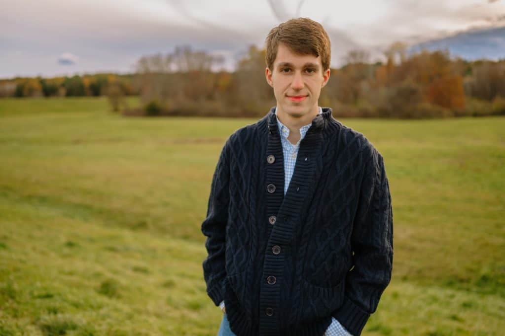 Student blogger Owen Fitzpatrick is smiling at the camera, standing on a grassy hill. 