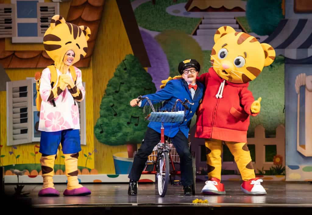 The cast of Daniel Tiger's Neighborhood on stage. Daniel Tiger receives a hug from Mr. McFeely while Mom Tiger looks on. 