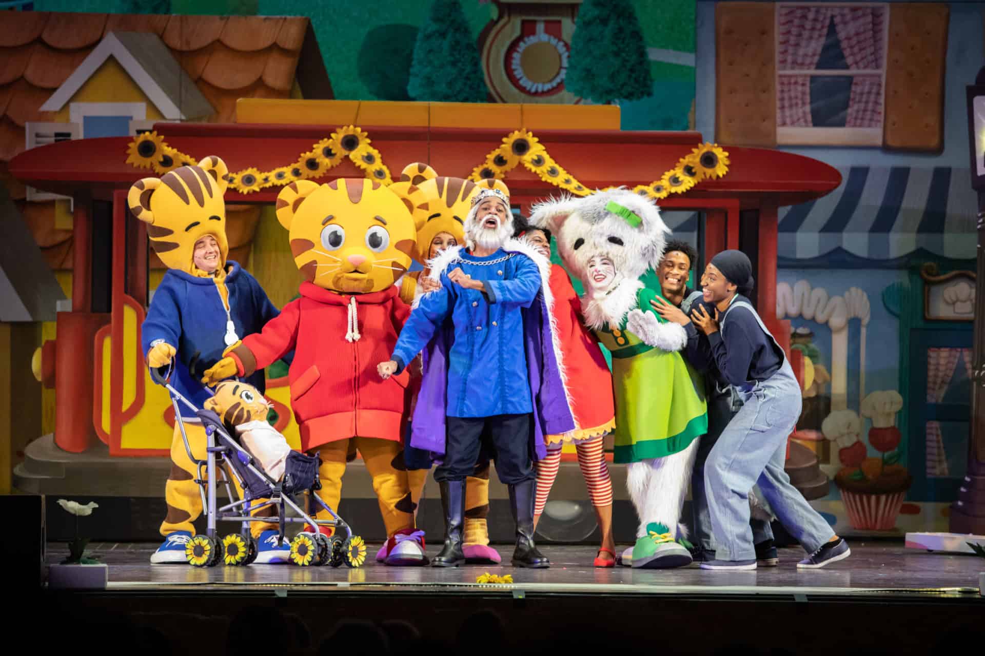 The cast of Daniel Tiger's Neighorhood Live! performs on stage. Some cast members are in full-body costumes for their characters, and some are wearing clothing costumes.