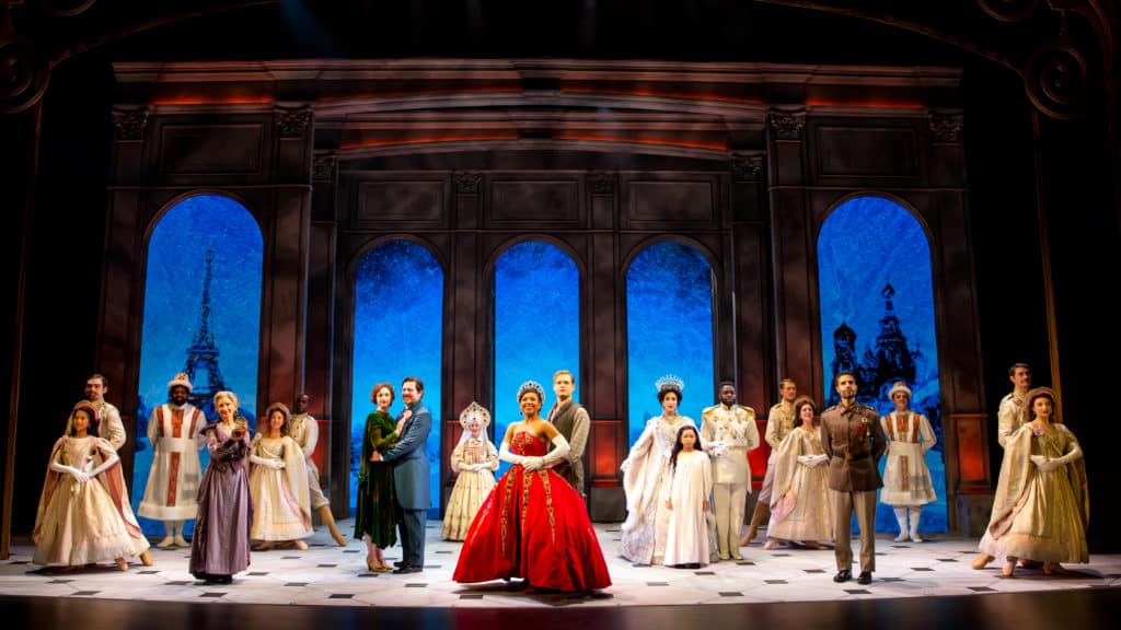 The cast of Anastasia is standing regally at the front of a stage, looking out into the distance. 