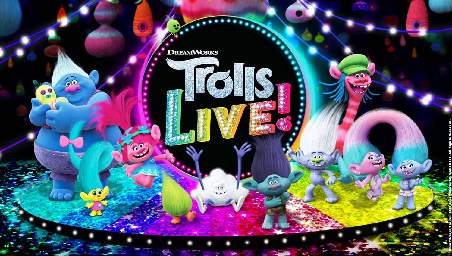 The logo for Trolls LIVE! featured on a black background. "Trolls LIVE" is written in colorful, rainbow text with a blue circle encompassing the words. The Trolls characters stand in front of and besides the words, and stand on a rainbow stage.