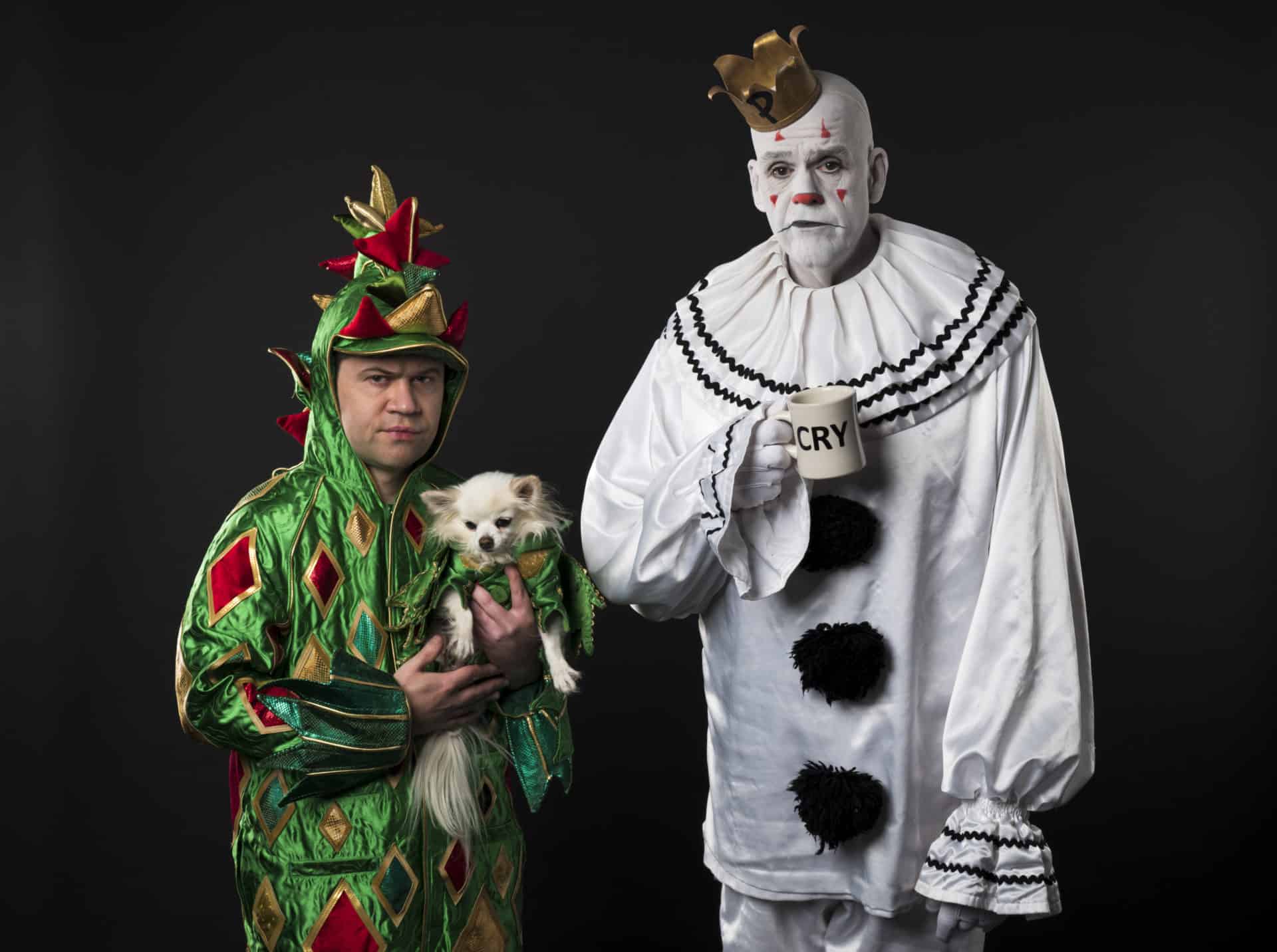 Piff the Magic Dragon stands in his green, scaly dragon skin costume holding his chihuahua, Mr. Piffles. Puddles Pity Party has white face paint on and a white clown outfit. He looks sad and is holding a mug that reads "Cry"