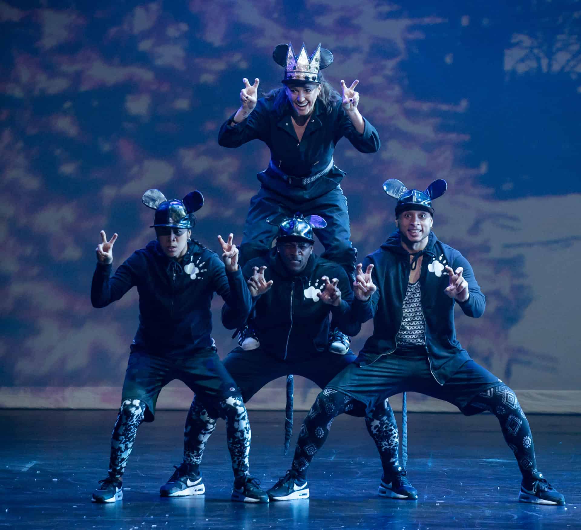 Four people stand and form a pyramid. They are all wearing rat ears on their hats and are making rat claws with their hands.