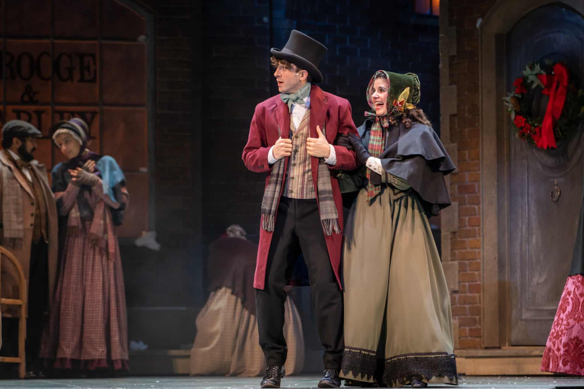 Tyler Bellmon and Laura D. DeGiacomo in A Christmas Carol. They were 1800s London winter outfits and Laura holds Tyler's arm.