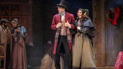 Tyler Bellmon and Laura D. DeGiacomo in A Christmas Carol. They were 1800s London winter outfits and Laura holds Tyler's arm.