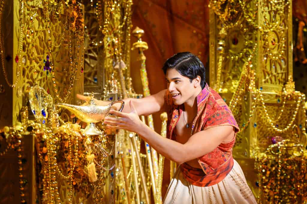 Aladdin reaches for the gold lamp in a pile of gold treasures.