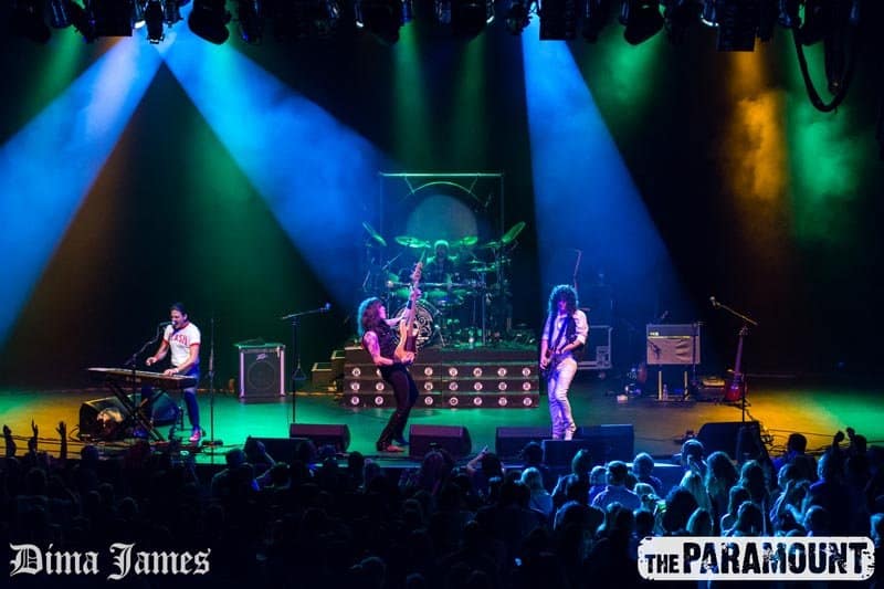 Almost Queen performing on stage. Randy Gregg stands in the center of the stage and holds his guitar upright.