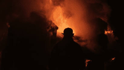 A firefighter stands in front of a burning fire