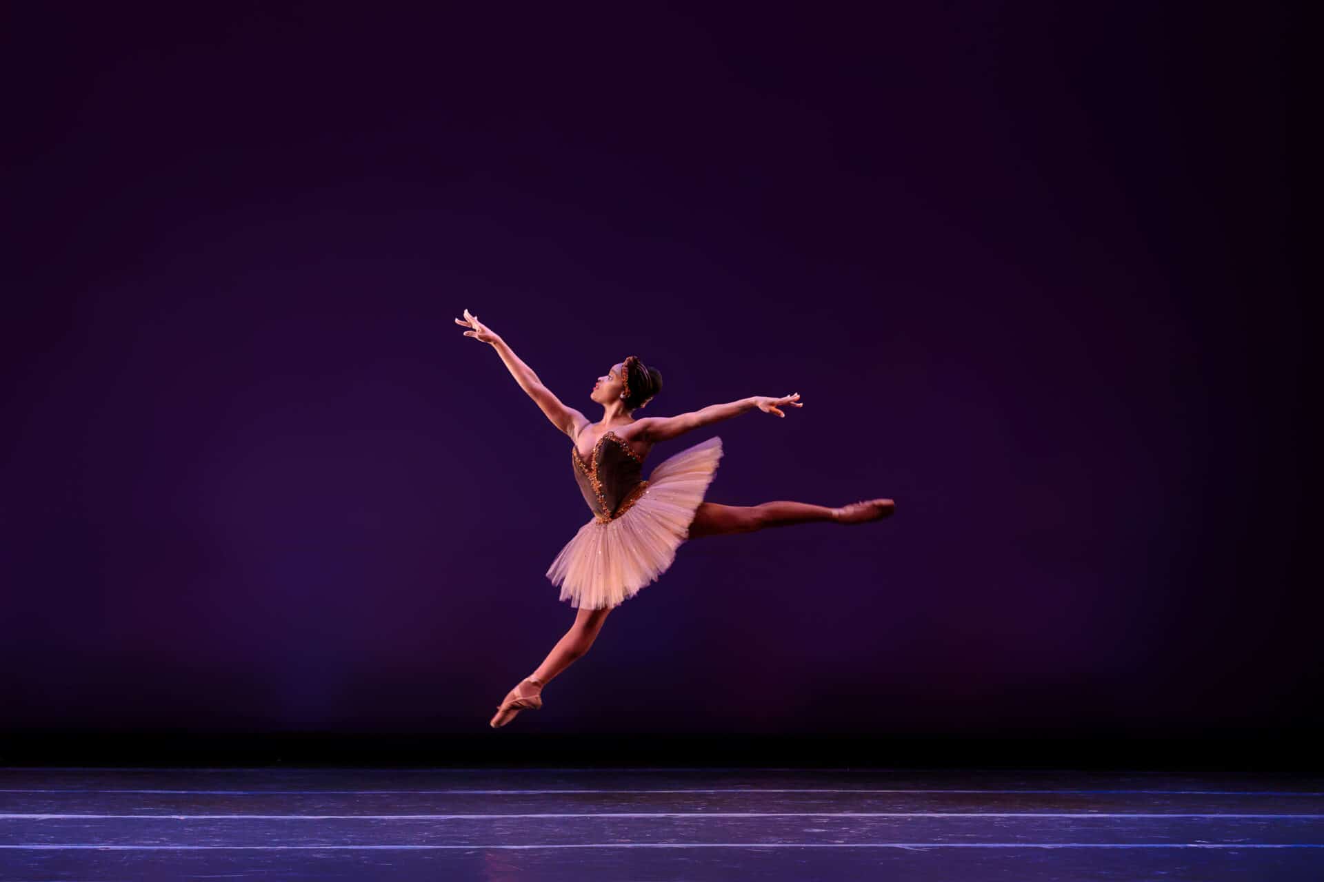 Ingrid Silva dances on stage and performs ballet. She dances in a pink tutu and dances in front of a purple backdrop.