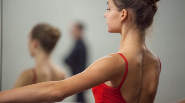 ballerina in a red leotard at the barre with her arm out