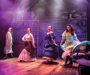 Four ladies hold their dresses as they dance in front of a bookshelf