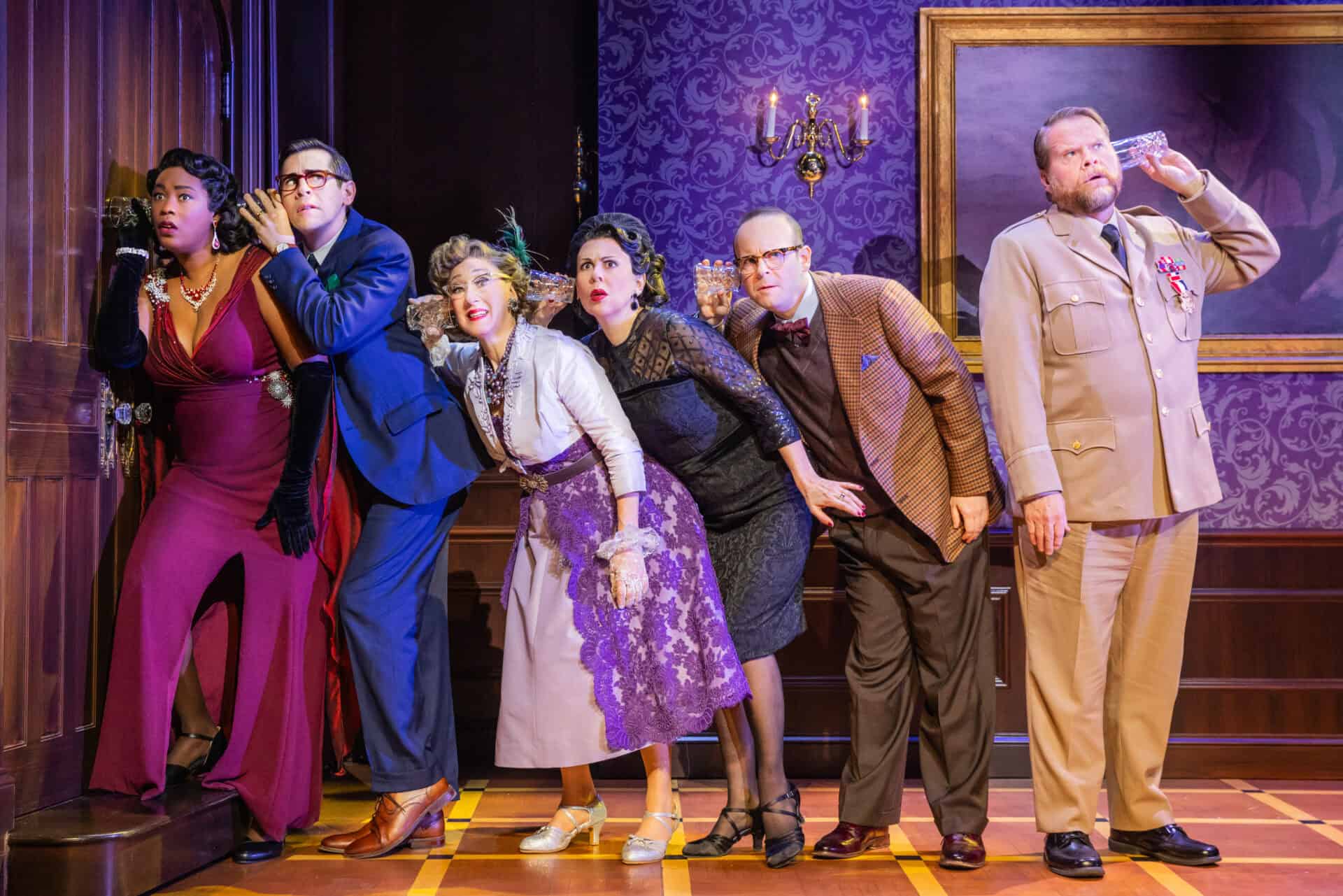 A scene from Clue where five main characters are lined up consecutively to the left of the stage, looking nervous while holding glasses to the back of the person in front of them. The sixth actor at the end of the line faces the right and hold his glass up to no one.
