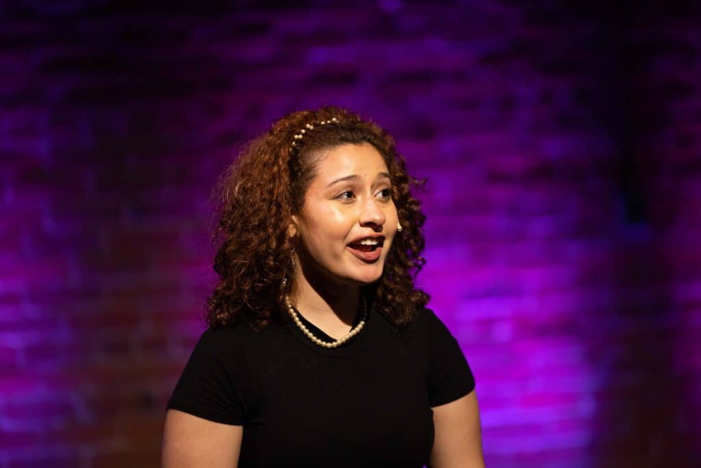 Alyssa, a WYSH 2023 participant, captured in a monologue onstage with purple lights behind her.