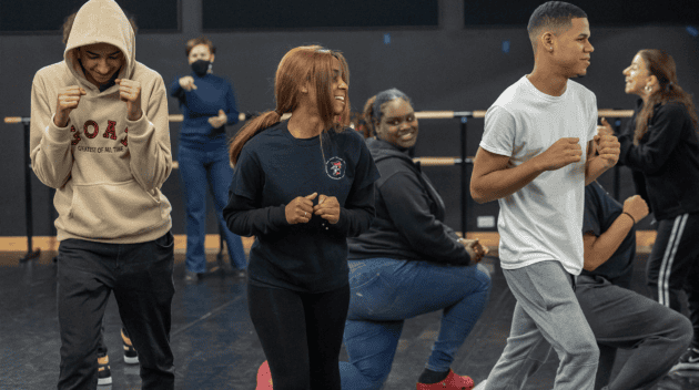 A candid photo during the Math in Choreography workshop. In the foreground are several students caught in different dance moves while instructors in the background give directions.