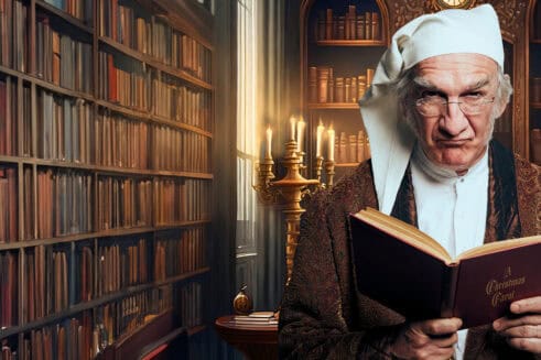 Ebenezer Scrooge is in a library, scowling and looking directly at the viewer, with an open copy of A Christmas Carol in his hands.