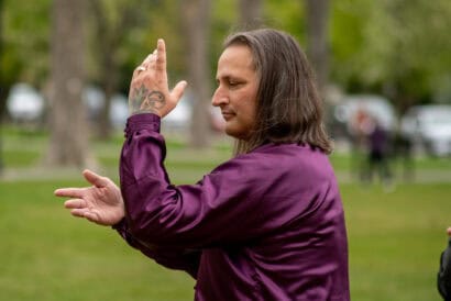 A tai chi instructor wearing a purple long sleeved shirt holds a pose while teaching in Francis R. Carroll Plaza.