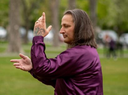 A tai chi instructor wearing a purple long sleeved shirt holds a pose while teaching in Francis R. Carroll Plaza.