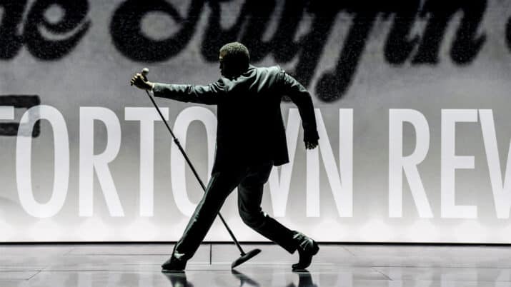 An actor from Ain't Too Proud: Life and Times of the Temptations onstage with their back to the camera, holding a mic stand angled off to the side.