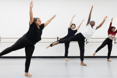 Four students in Modern II (Ages 15+) photographed mid-move with their arms up and leaning to one side while balancing on one foot.