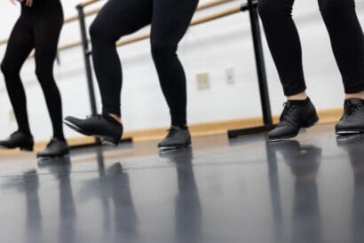 The legs of three tap dancers in Primary Tap II (Ages 10-12), all with black leggings and tap shoes.