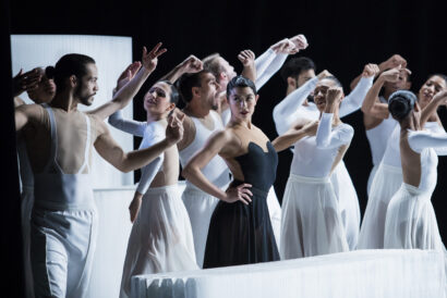 Ballet Hispánico in CARMEN.maquia. Photo by Marius Fiskum/Northern Lights Festival - Hanover Theatre and Conservatory A female dancer dressed in all black poses defiantly surrounded by several dancers dressed in all white