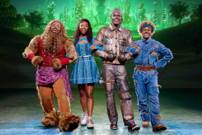 WIZ_1920 x 1080 hero image - video card - FB event - Hanover Theatre and Conservatory Four cast members from the national tour of The Wiz pose arm-in-arm onstage in colorful costumes, with a glowing Emerald City backdrop behind them.