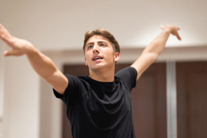 Acting for the Camera Grades 8-12 - Hanover Theatre and Conservatory Young man in a black t-shirt stretches with arms extended upward in an indoor setting