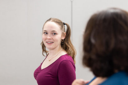 Adult Acting for the Camera Ages 18+ - Hanover Theatre and Conservatory Young woman in a magenta top speaks smiling at someone off-camera in a neutral room.
