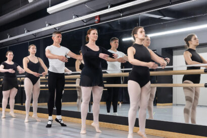 Adult Ballet Intermediate Ages 18+ SUMMER - Hanover Theatre and Conservatory Group of ballet dancers at a mirrored barre, practicing arm positions in a studio wearing black leotards and light tights.