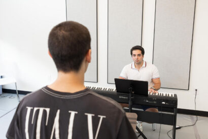 Adult Choral and Solo Singing Ages 18+ - Hanover Theatre and Conservatory Two men in a music studio: one seated at a Roland keyboard facing the other man standing nearby, white walls and sound panels behind them.