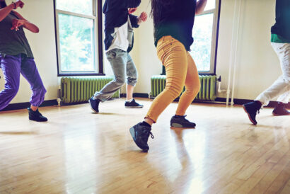 Hip Hop SUMMER - Hanover Theatre and Conservatory Group of people dancing in a bright studio, showing colorful pants and sneakers in mid-motion by large windows.