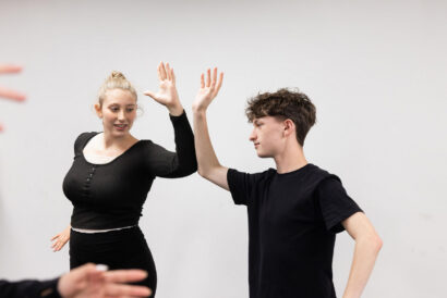 Introduction to Classic Comedy Grades 9-12 - Hanover Theatre and Conservatory Two young adults in black shirts high-five each other in a bright studio setting.
