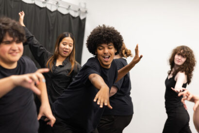 Lets Make A Musical Grades 8-12 - Hanover Theatre and Conservatory Group of diverse young people dancing in a studio, wearing black shirts, with energetic arm movements and smiles.