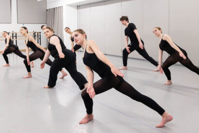 Modern Foundations SUMMER - Hanover Theatre and Conservatory Group of dancers in black outfits practicing a choreographed pose in a ballet studio with mirrors and ballet barres in the background.