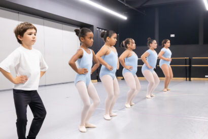 Pre-Ballet SUMMER - Hanover Theatre and Conservatory Young boy in a white shirt leads a line of girls in pale blue leotards during a ballet class in a studio.",