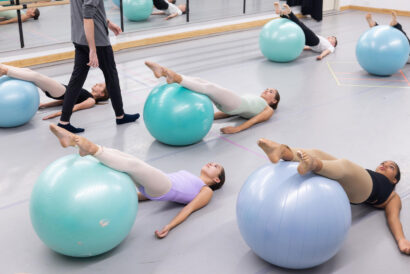 Progressing Ballet Technique Junior SUMMER - Hanover Theatre and Conservatory Group of people in a studio using large exercise balls for leg raises; instructor stands nearby.